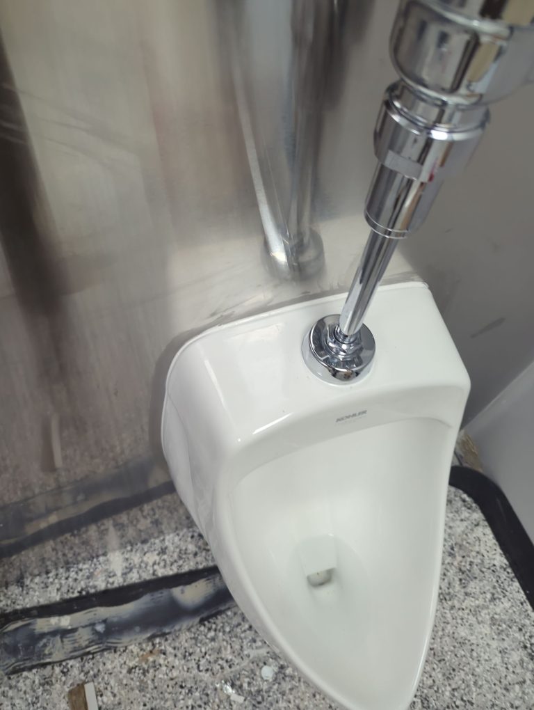 Close-up of a urinal flush valve and chrome supply pipe