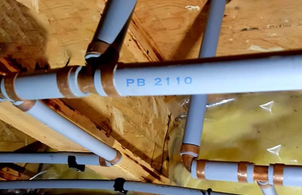 Gray polybutylene water pipe stamped PB 2110 with copper crimp ring fittings under a floor