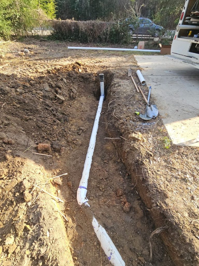 New PVC sewer line laid in an open trench next to a driveway