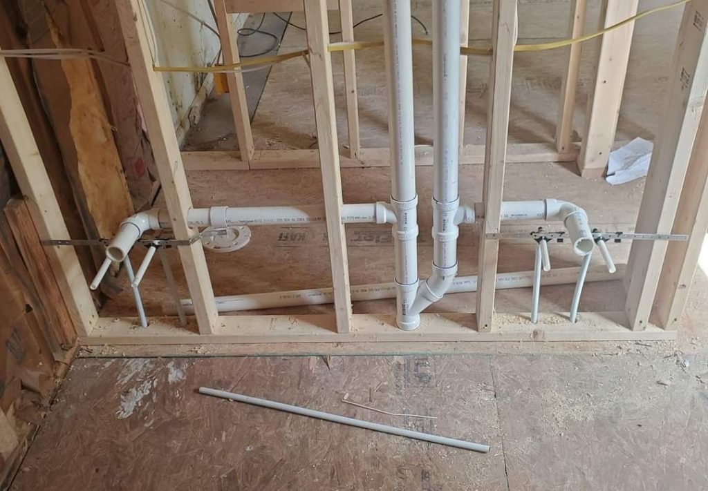 New plumbing rough-in with PVC drain pipes and supply stub-outs in wall framing