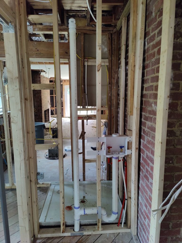 New PEX water supply lines and PVC drain rough-in beside a brick wall during a home remodel